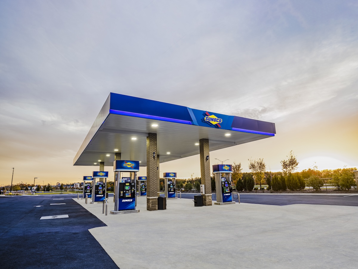 Sunoco gas station at sunrise with bright canopy lighting and multiple fuel pumps on a clean concrete lot.